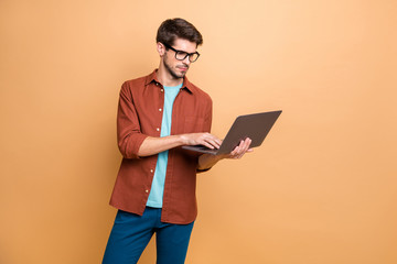Portrait of his he nice attractive serious successful smart clever focused concentrated brunette guy holding in hands laptop browsing isolated over beige color pastel background