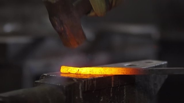 Close up of hammer striking molten iron billet lying on anvil