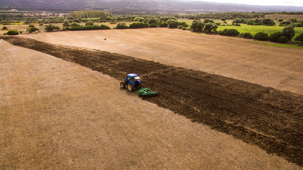 aerial view drone of blue tractor with plow in operation in the field