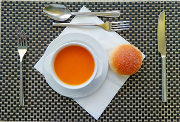 Top view of table setting with pumpkin soup, bun, cutlery and white paper napkin