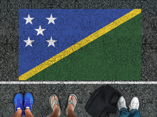 people legs are standing on asphalt road next to flag of Solomon Islands and border