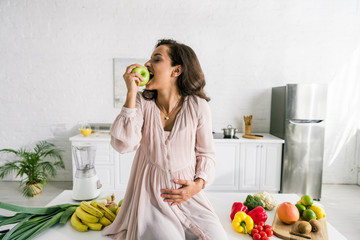happy pregnant woman eating apple near food on table