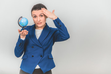 Young geography teacher holding a globe, keeping hand on the head, looking at the camera confused...