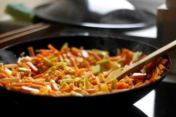 Cooking carrot, pumpkin, zucchini nad leek in wok. Selective focus, close-up.