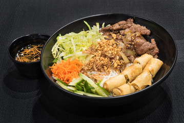 Rice noodles with grilled meat and spring roll, a popular Vietnamese cold rice vermicelli. Vietnamese cuisine.