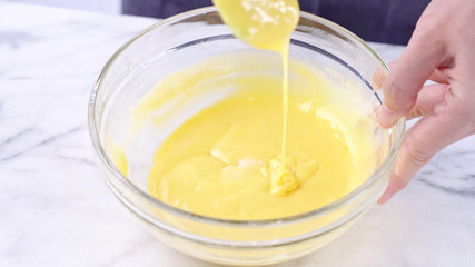 Mixing egg yolk into cake batter with green rubber spatula mixer tool stirring until smooth and blend well in a glass bowl, close up, lifestyle
