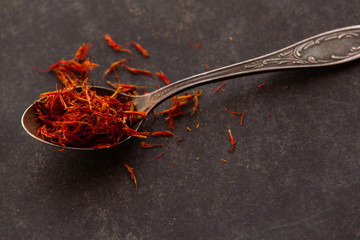 Aromatic condiment saffron in a spoon on dark background.
