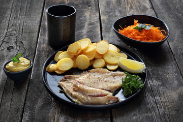 Grilled fish fillet served with baked potatoes, carrot salad and sauce