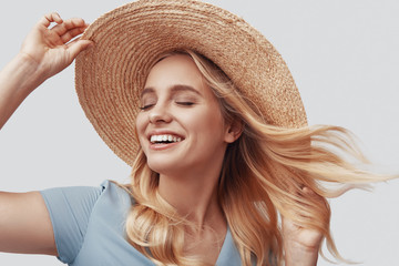 Attractive young woman smiling and keeping eyes closed while standing against grey background