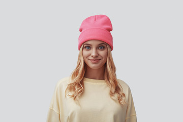 Attractive young woman looking at camera and smiling while standing against grey background