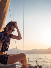 attractive young woman in a striped t-shirt enjoys the sunset on the deck of a sailing yacht....