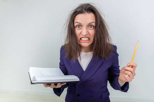 Insane young teacher with tousled hair, holding notebook and pen, setting her teeth, looking out of mind.