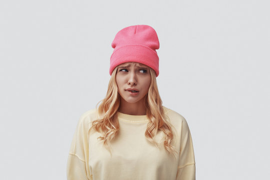 Sad young woman making a face and looking away while standing against grey background