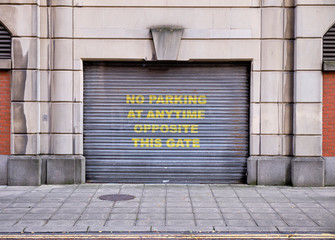 Minimal symetric building facade with a metal sliding door garage with large yellow writing 