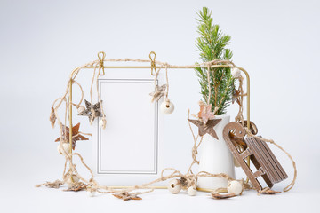 Little fir tree in ceramic vase and golden frame on white background. Christmas card - toys, garlands and wooden thinks.