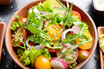 Top view at Clay dish with vegetable salad of lettuce, cherry tomatoes, radish, cucumber, onion and basil on slate tray