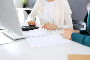 Accountant checking financial statement or counting by calculator income for tax form, hands close-up. Business woman sitting and working with colleague at the desk in office. Audit concept