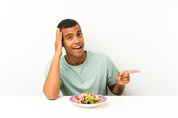 Young handsome man with salad in a table surprised and pointing finger to the side