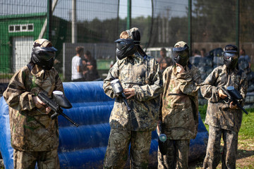 Paintball game. Warriors in protective suits. Training ground. Masks on the faces. Marker shooting.