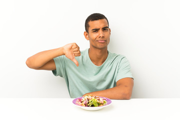 Young handsome man with salad in a table showing thumb down sign