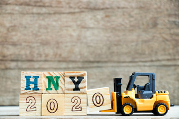 Toy yellow forklift hold letter block 0 to complete word HNY 2020 (Abbreviation of Happy new year) on wood background