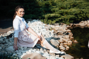 Outdoor photo of beautiful girl with braided braids. Girl in school uniform. Girl sits by the river