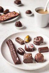 Coffee cup and assortment of fine chocolate candies on light grey stone background. 