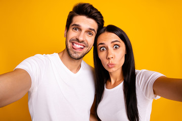 Obraz premium Photo of two people in foolish mood taking selfies sticking tongue making faces wear casual clothes isolated yellow color background