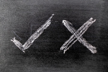 White color chalk hand drawing as check mark of right and wrong shape on black board background