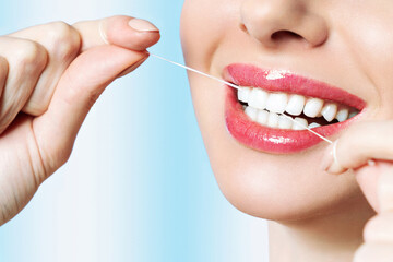 Young beautiful woman is engaged in cleaning teeth. Beautiful smile healthy white teeth. A girl holds a dental floss. The concept of oral hygiene.