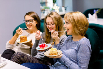 Three young beautiful Women sitting on the sofa in cafe indoors and Having lunch In Cafe. Women eating cakes and having fun