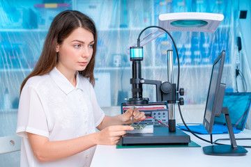 Young woman in inspection electronics PCB devise. Modern electronics laboratory