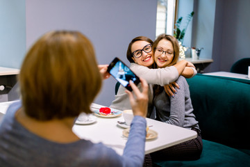 Women friends in cafe indoors. Two pretty women friends hugging and posing for the photo together,...