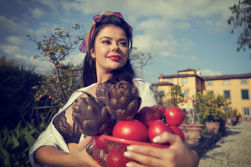 La dolce vita lifestyle. An Italian woman is carrying a basket with vegetables. House and garden in...
