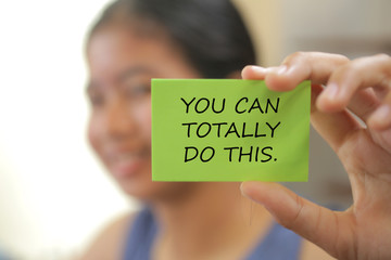 Blurry image of young girl holding a motivation sign with text on it - you can totally do this. ...