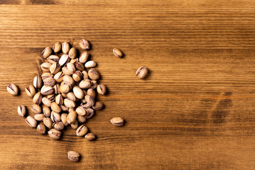 Pile of unpeeled salted pistachios on a wooden table, top view, copy space. Beer snack.