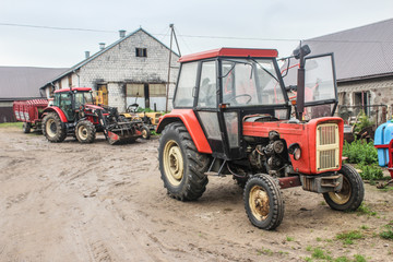 Red tractors and agricultural equipment in the courtyard of a dairy farm. A cowshed in the background.Close up. Podlasie, Poland.