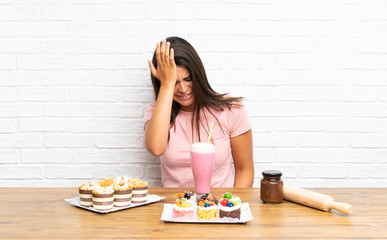 Young girl with lots of different mini cakes having doubts with confuse face expression