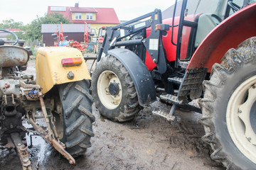 Yellow and red tractors  in the courtyard of a dairy farm. View from the back. Apartment building in the background. Podlasie, Poland.