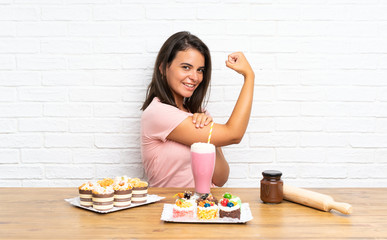 Young girl with lots of different mini cakes making strong gesture