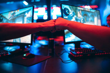 Professional gamer greeting and support team fists hands online game in neon color blur background. Soft focus, back view - obrazy, fototapety, plakaty