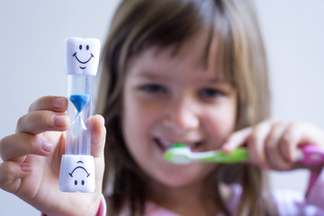 Child measures time while brushes her teeth. Healthy habits, dentalcare concept. Close up.