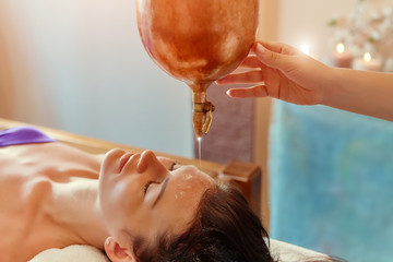 ayurveda massage alternative healing therapy.beautiful caucasian female getting shirodhara treatment lying on a wooden table in India salon. - obrazy, fototapety, plakaty