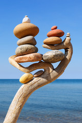 Multicolored balanced stones on an wooden snags, on a blue sky and sea background