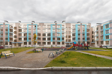 Exterior of new modern low-rise house building exterior mixed-use urban multi-family residential district area development with playing field and benches for rest in foreground overcast autumn day.