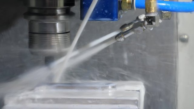 Close up of working CNC milling machine spindle with tool holder and a cutter spinning fast and cutting metal part while getting three jets of coolant.