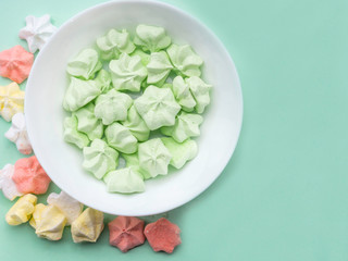 Colorful mint, coral color, and yellow meringues on pastel green table. Many trendy top view dessert image. Bakery products background, sweet dessert.