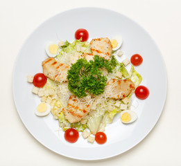 Caesar salad with chicken on a white plate and on a white background, top view.
