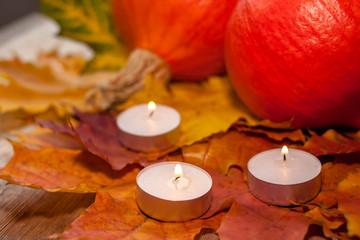 Fototapeta na wymiar Composition with pumpkins and candles on maple leaves on wooden background. Side view. Selective soft focus.