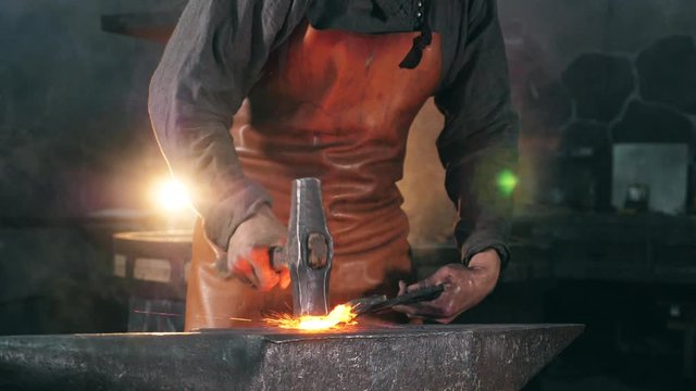 Craftsman is forging iron tool in the smithy